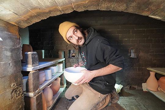 man with hat inside pottery kiln with some pots